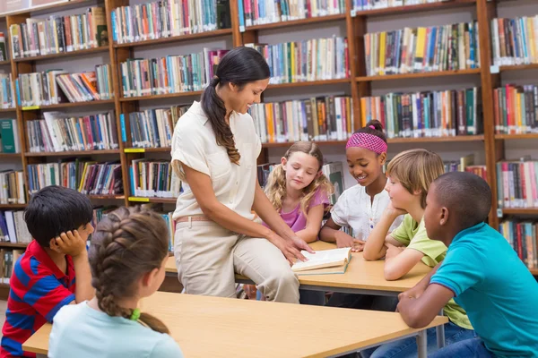 Милые ученики и чтение учителей в библиотеке — стоковое фото