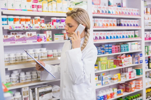 Pharmacy intern phoning while reading clipboard — Stock Photo, Image