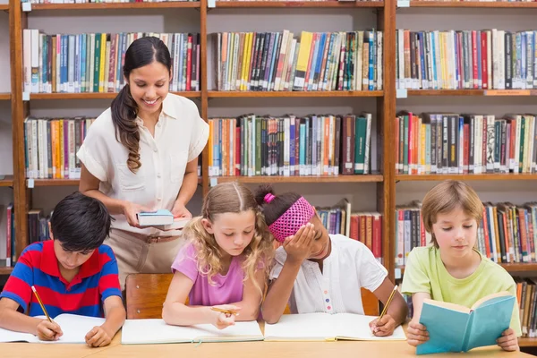 Mooie leraar helpt leerlingen in bibliotheek — Stockfoto