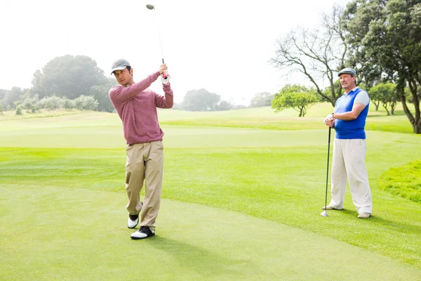 Golfspelare svängande sin klubb med vän bakom honom — Stockfoto