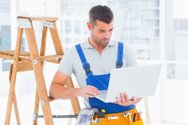 Repairman using laptop by ladder in office — Stock Photo, Image