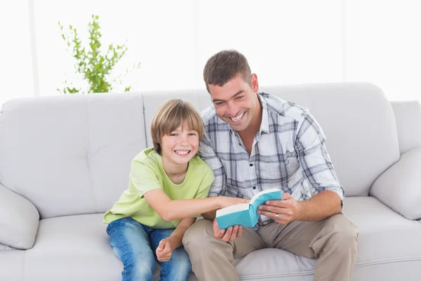 Vater und Sohn sitzen mit Bilderbuch auf Sofa — Stockfoto