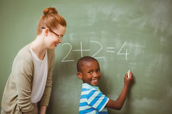 Teacher assisting boy to write on blackboard in classroom — Stock Photo, Image