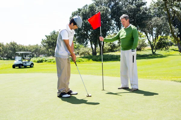 Golfista držení vlajky otvor pro přítele uvedení míč — Stock fotografie