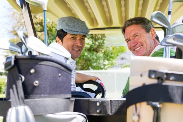 Golffreunde fahren im Golfbuggy lächelnd in die Kamera — Stockfoto