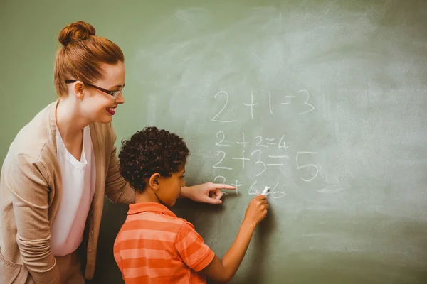 Leraar bijstaan jongen te schrijven op blackboard in klas — Stockfoto