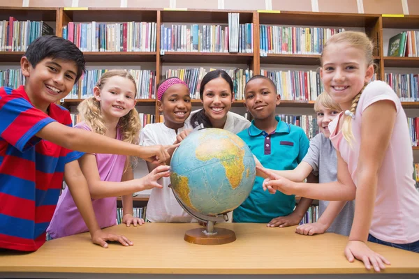 Ładny uczniowie i nauczyciel patrząc na świecie w bibliotece — Zdjęcie stockowe