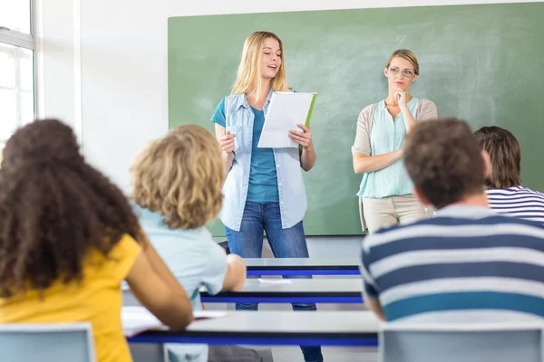 Student explaining notes besides teacher in class — Stock Photo, Image