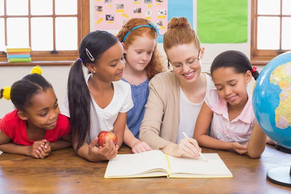 Cute pupils and teacher smiling at camera in classroom — Stock Photo, Image