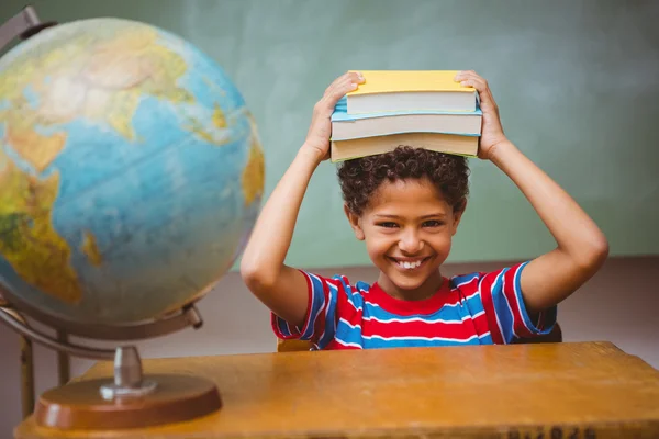 Niño pequeño sosteniendo libros sobre la cabeza en el aula —  Fotos de Stock