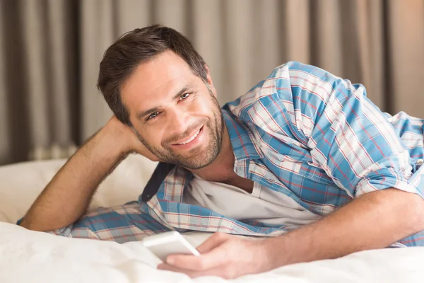 Homem relaxante na cama usando seu telefone — Fotografia de Stock