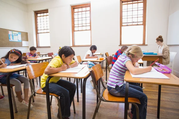 可爱的学生坐在教室里的桌子上写 — 图库照片