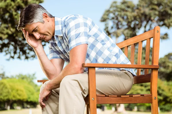 Расстроенный мужчина сидит на скамейке в парке — стоковое фото