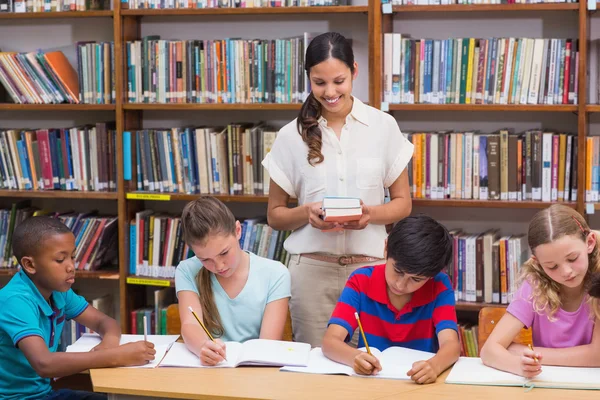 Graziosa insegnante aiutare alunni in biblioteca — Foto Stock