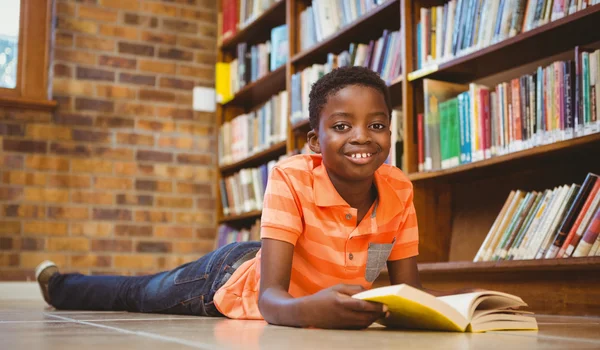 Cute boy reading book in library — Stock Photo, Image