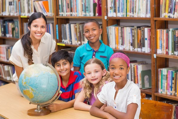 Lindos alumnos y profesores mirando el globo en la biblioteca — Foto de Stock