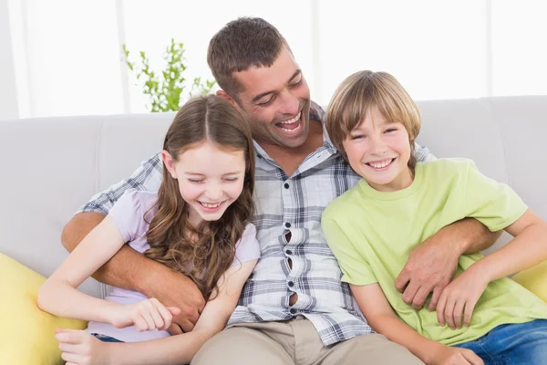 Father tickling children while sitting on sofa — Stock Photo, Image