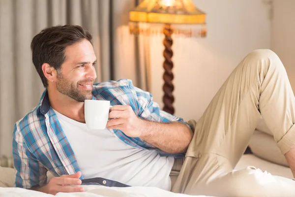 Adam yatakta sıcak bir içecek ile rahatlatıcı — Stok fotoğraf