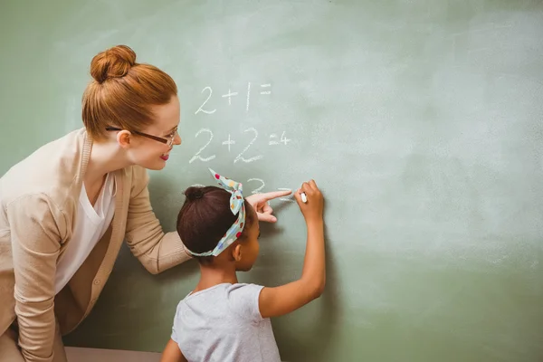 Leraar bijstaan meisje om te schrijven op blackboard in klas — Stockfoto