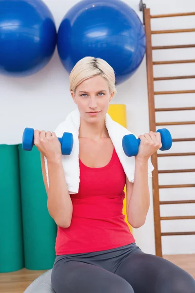 Blondine hebt Hanteln auf Gymnastikball — Stockfoto