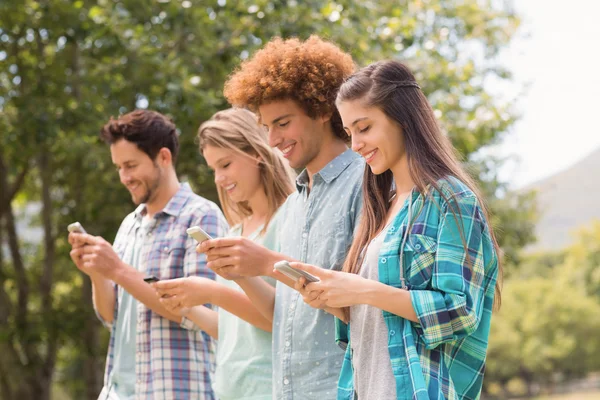 Happy vänner i parken använder sina telefoner — Stockfoto