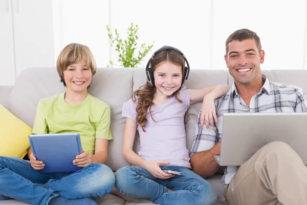 Homem feliz com crianças usando tecnologias no sofá — Fotografia de Stock