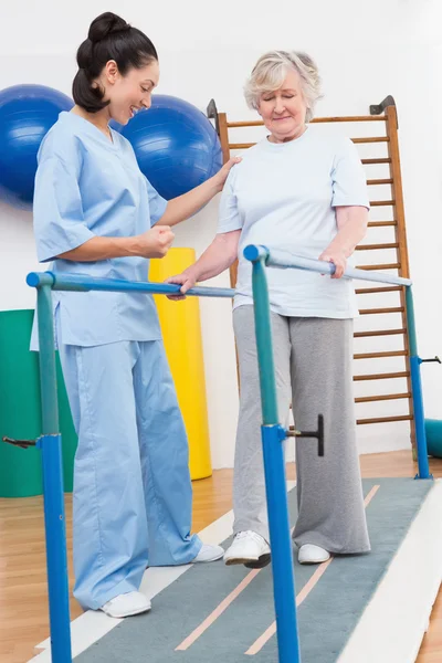 Mulher idosa caminhando com barras paralelas com terapeuta — Fotografia de Stock