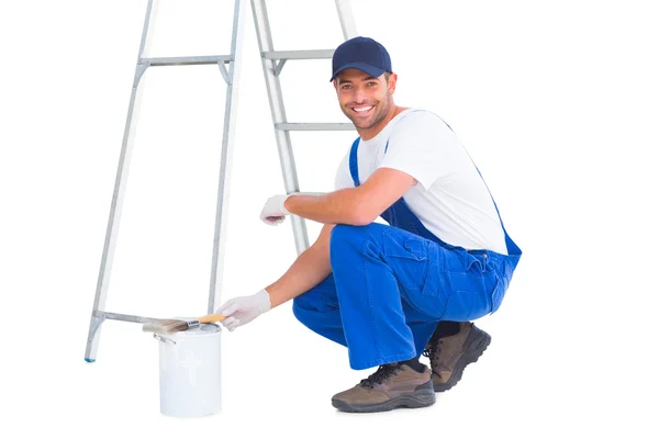 Happy handyman crouching by paint can — Stock Photo, Image