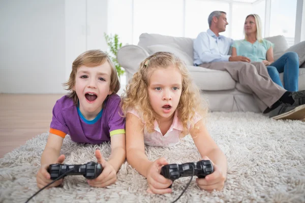 Irmãos jogando videogame enquanto os pais sentados no sofá — Fotografia de Stock