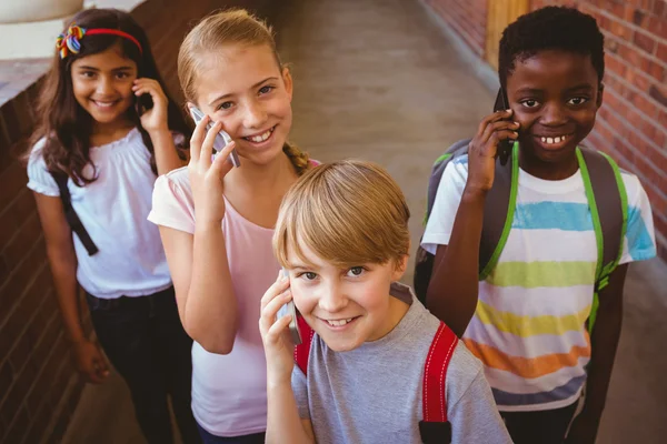 Écoliers utilisant des téléphones cellulaires dans le couloir scolaire — Photo