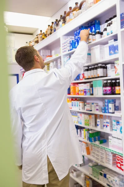 Farmacéutico en bata de laboratorio tomando frasco de estante —  Fotos de Stock