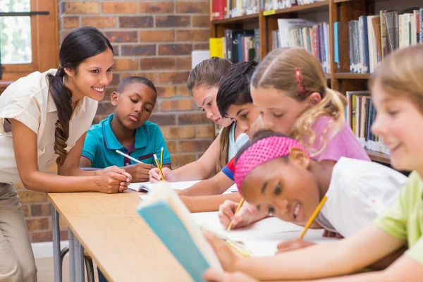 Pretty teacher helping pupils in library — Stock Photo, Image