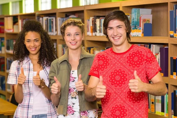 Högskolestudenter gestikulerande tummen upp i biblioteket — Stockfoto