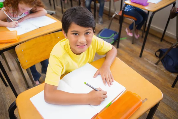 Cute pupils drawing at their desks one smiling at camera Royalty Free Stock Images