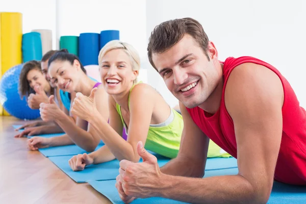 Friends gesturing thumbs up while lying on mats at gym — Stock Photo, Image