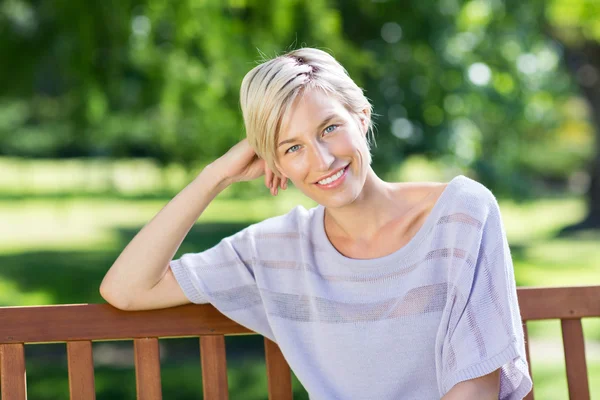 Uśmiechnięta blondynka siedzi na ławce — Zdjęcie stockowe
