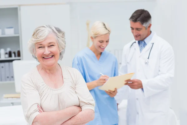 Пациент улыбается, когда доктор и медсестра обсуждают — стоковое фото