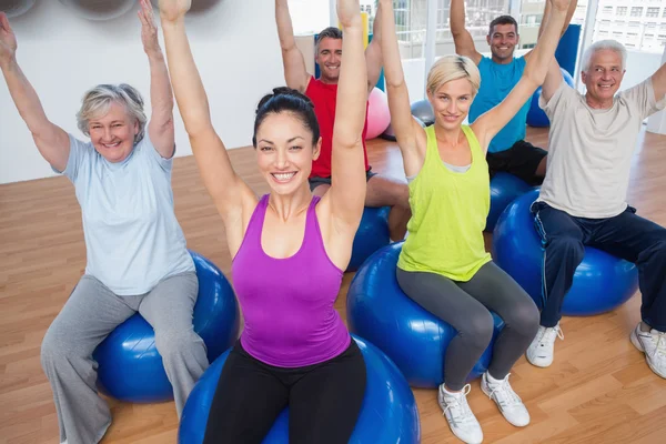 Pessoas sentadas em bolas de exercício com as mãos levantadas — Fotografia de Stock