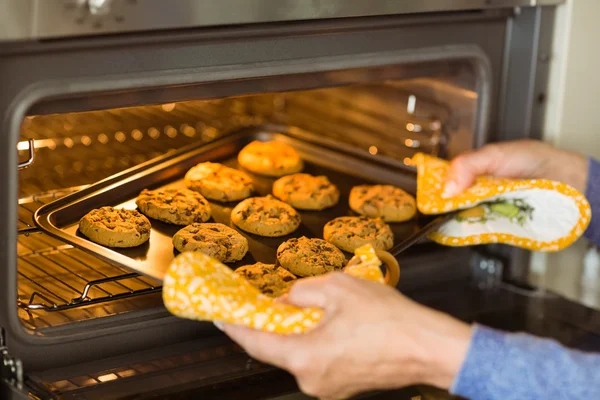 Woman taking tray of cookies out of oven — Stock Photo, Image