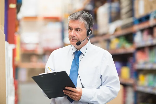 Gerente de armazém usando headset escrita na área de transferência — Fotografia de Stock