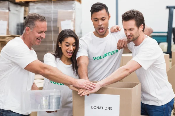 Volontär team hand i hand på en låda med donationer — Stockfoto