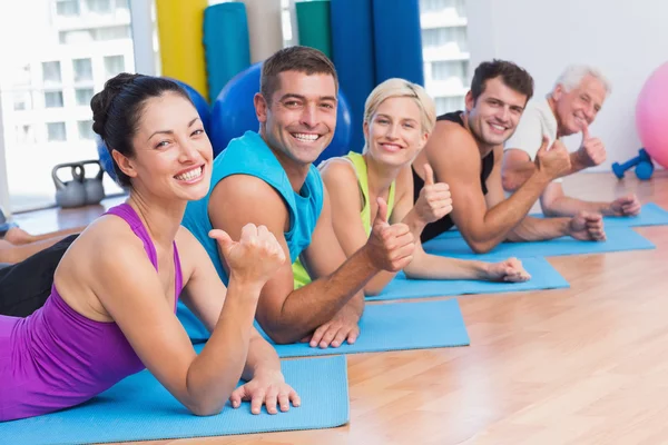 Mensen gebaren duimen omhoog terwijl liggend op matten op sportschool — Stockfoto