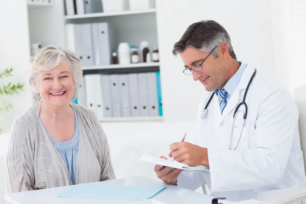 Médico escribiendo prescripción mientras paciente —  Fotos de Stock