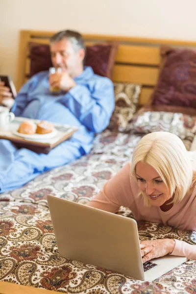 Happy mogen blondin med laptop på sängen — Stockfoto