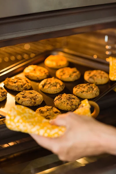 Woman taking tray of cookies out of oven — Stock Photo, Image