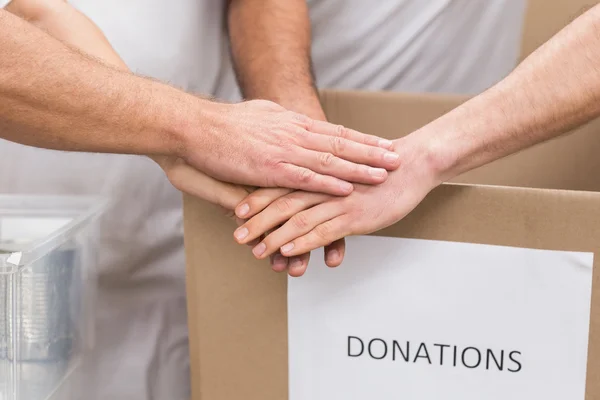 Volontär team hand i hand på en låda med donationer — Stockfoto