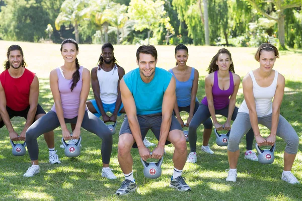 Grupo de fitness en cuclillas en el parque con campanas de caldera —  Fotos de Stock