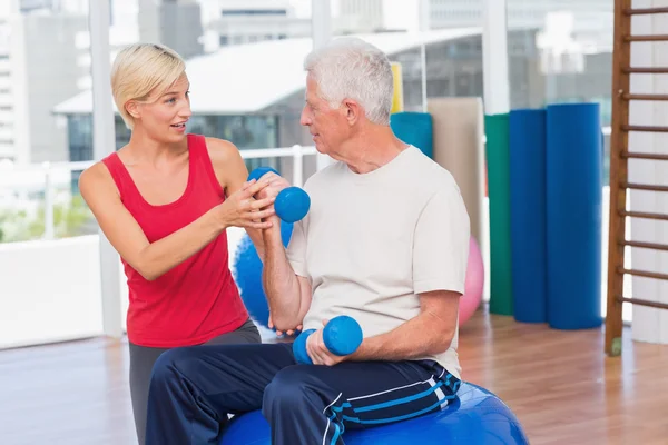 Female trainer assisting senior man in lifting dumbbells — Stock Photo, Image