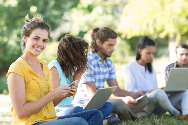 Amici sorridenti che utilizzano dispositivi multimediali nel parco — Foto Stock