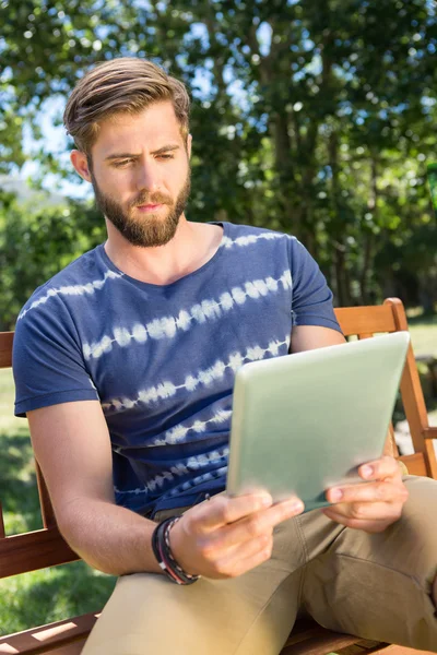 Young man using tablet on park bench — Stock Photo, Image